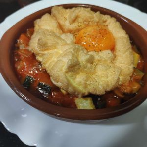 una cazuelita de barro con huevos souflé en su interior sobre una cama de pisto o sanfaina