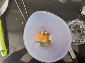 un recipiente con huevos y ajo cortado para batir y hacer alioli