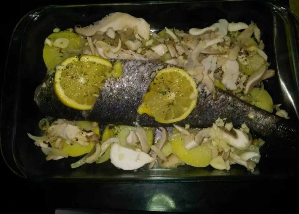 una font de forn transparent amb un llit de patates i ceba i corvina.