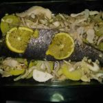 una bandeja de horno y encima de un lecho de patatas y cebolla una corvina encima con limón