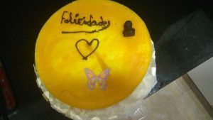 un pastís rodó de mousse de màngo decorat, amb felicitats de xocolata i una papallona comestible