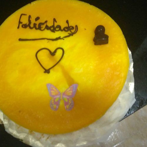 una tarta redonda de mousse de mango decorada, con felicidades de chocolate y una mariposa comestible