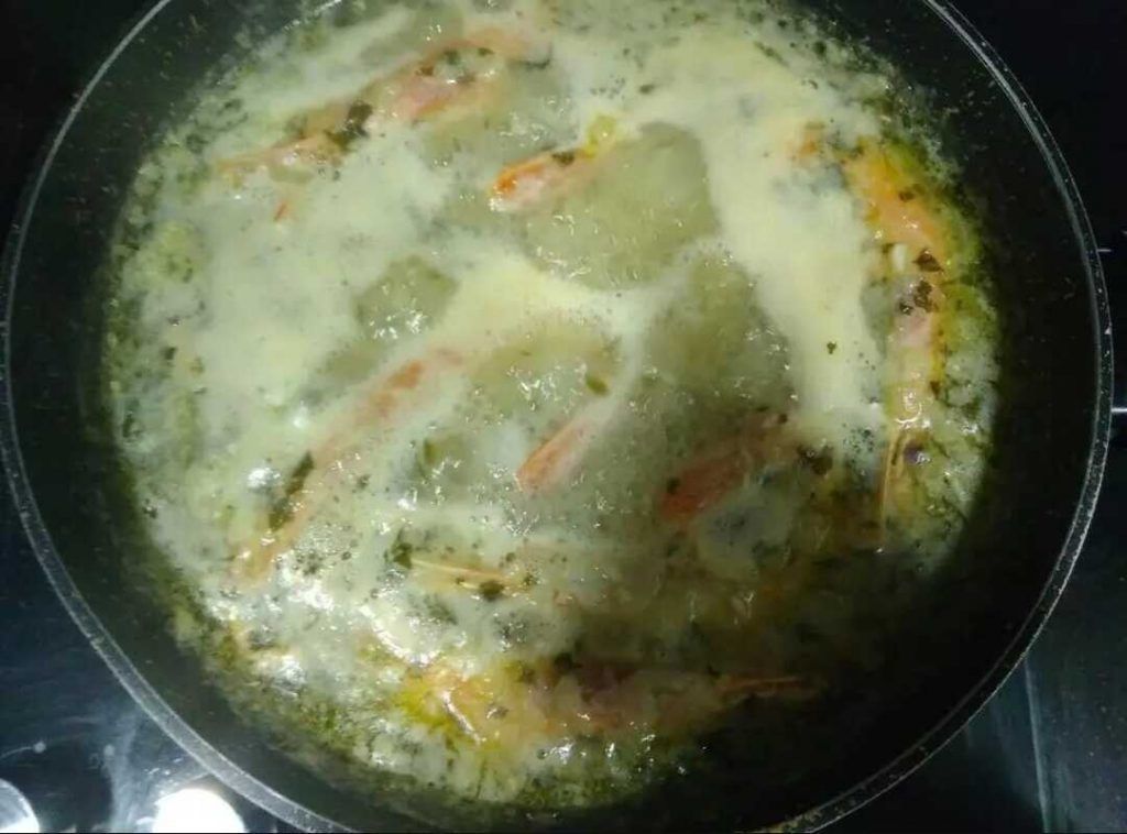 cociendo con el caldo y las gambas par la merluza en salsa verde