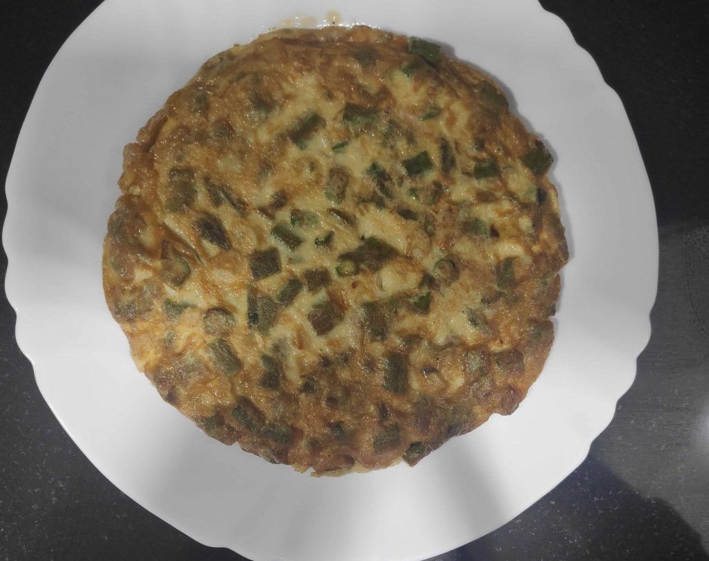 una tortilla de verduras en un plato blanco, sobre fondo mármol negro.