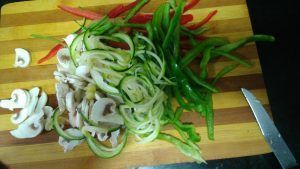 sobre una tabla de cortar de madera, las verduras cortadas en juliana pimientos,ebolla, champiñones laminados