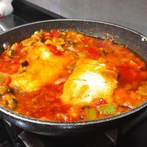 en una sartén dos lomos de bacalao cocinándose sobre la sanfaina