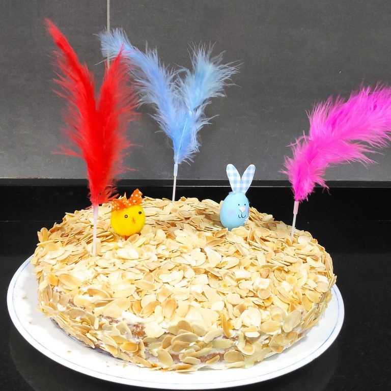 mona de pascua adornada con plumas de colores en un bizcocho de almendras.