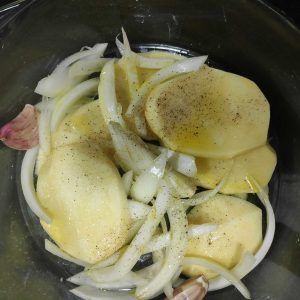 patatas y cebolla salpimentados en una fuente de horno para hornear el codillo