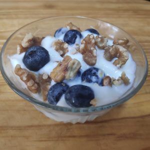 postre en un bol yogur, arándanos y nueces sobre fondo de madera