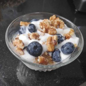 un bol con un postre de yogur, nueces y arándanos