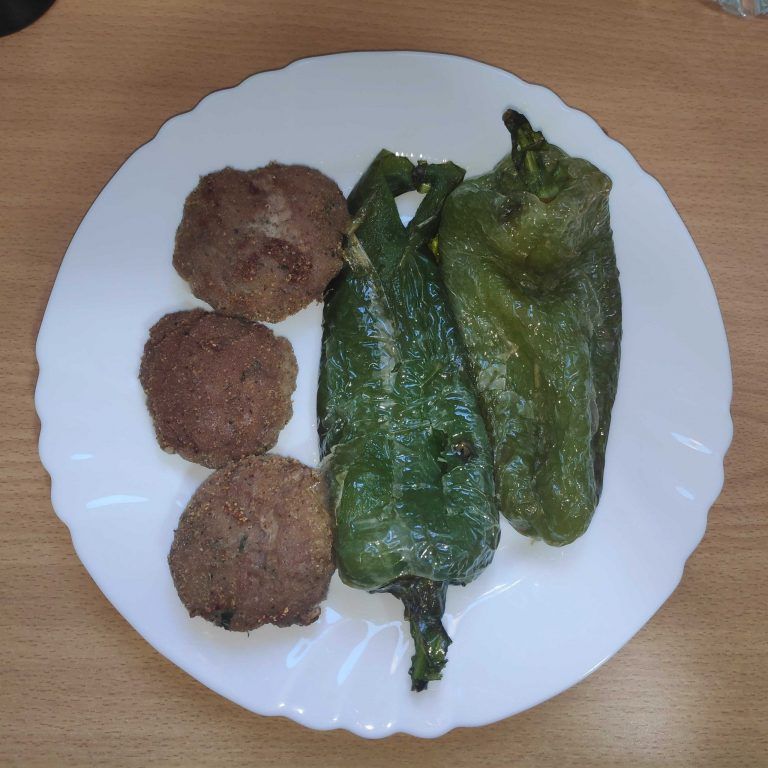 en un plato tres filetes rusos acompañados de pimientos verdes fritos