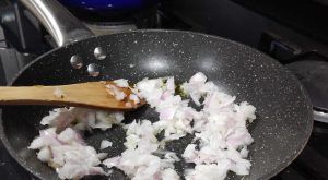cebolla en la sartén para elaborar la salsa de los pimientos del piquillo rellenos de merluza