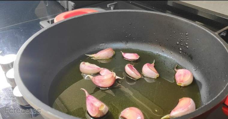 ajos en una cazuela con aceite, ajos con piel una cabeza de ajos