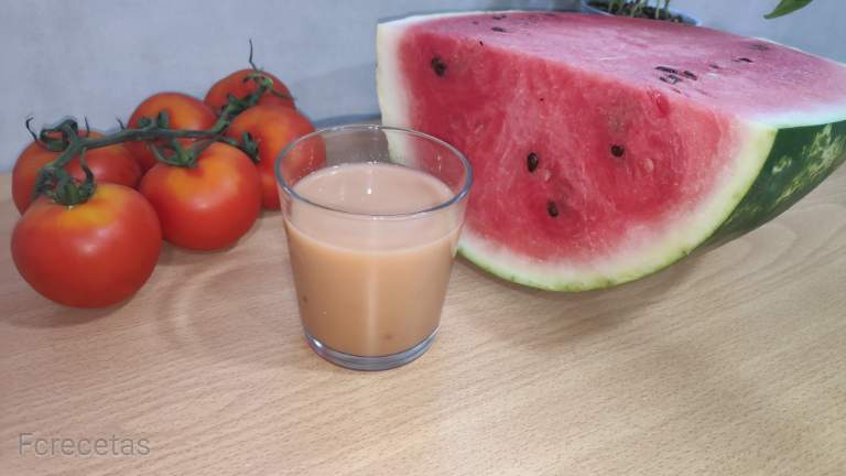 Gazpacho de sandía en un vaso con tomates y sandía alrededor en una mesa