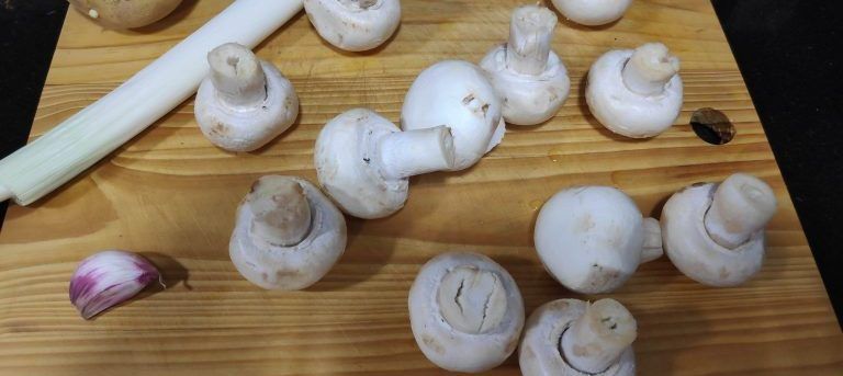 ingredientes de la crema de champiñones en una tabla de madera, champiñones, media cebolla, un puerro, un ajo, patata