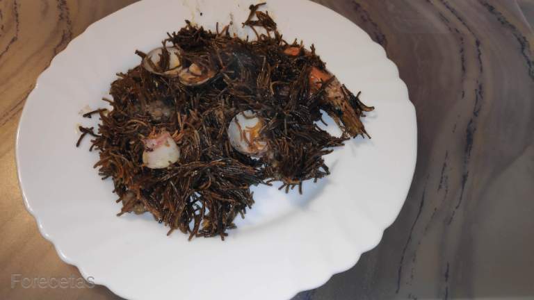 un plato blanco con fideuá negra de calamar y pescado.