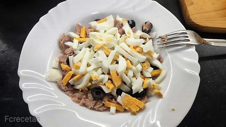 un plato blanco con atún, huevo y olivas troceadas