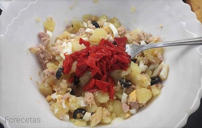 un plato con patata, atún, huevo duro, olivas y pimientos del piquillo troceado