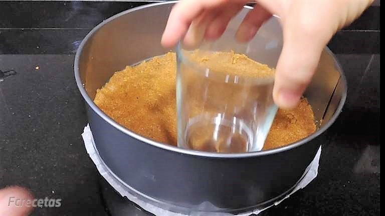 con un vaso aplanando la base de galleta en un molde redondo