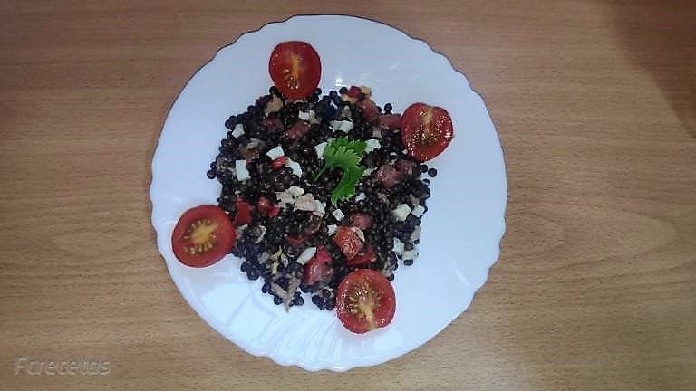 ensalada de lentejas beluga decorada con tamate cherry en un plato blanco