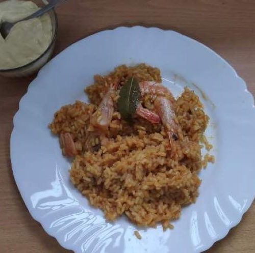 arròs a banda amb allioli en un plat blanc l'allioli en una salsera i tot sobre una taula de fusta