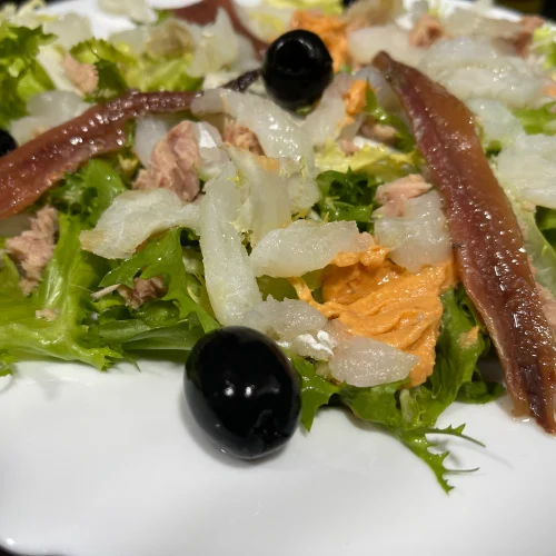 un plato con ensalada xatonada con escarola, bacalao, olivas negras,, y salsa