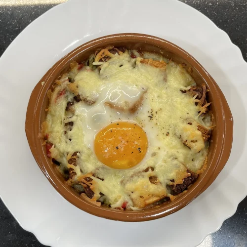 una ració d'ous napoleó en una cassola individual de fang sobre un plat blanc