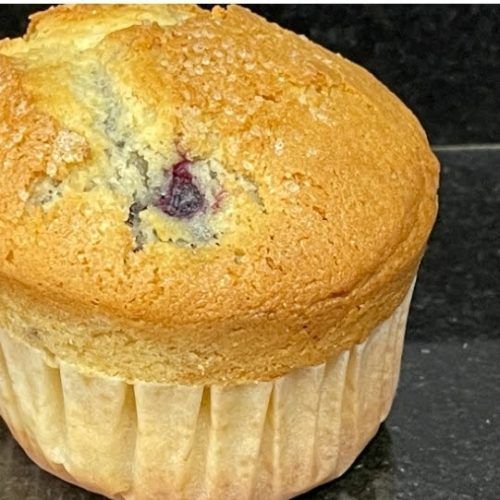 sobre fondo negro, un muffin o magdalena de moras con su papel blanco