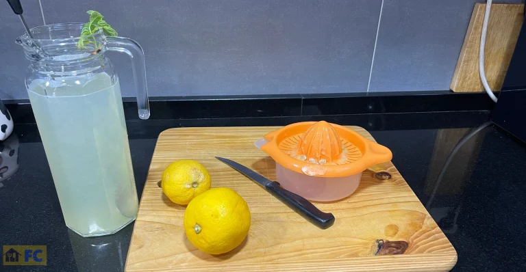 Dos limones, un exprimidor y una jarra con limonada y una ramita de hierbabuena