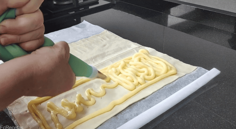 con una manga pastelera rellenando con crema la coca de hojaldre