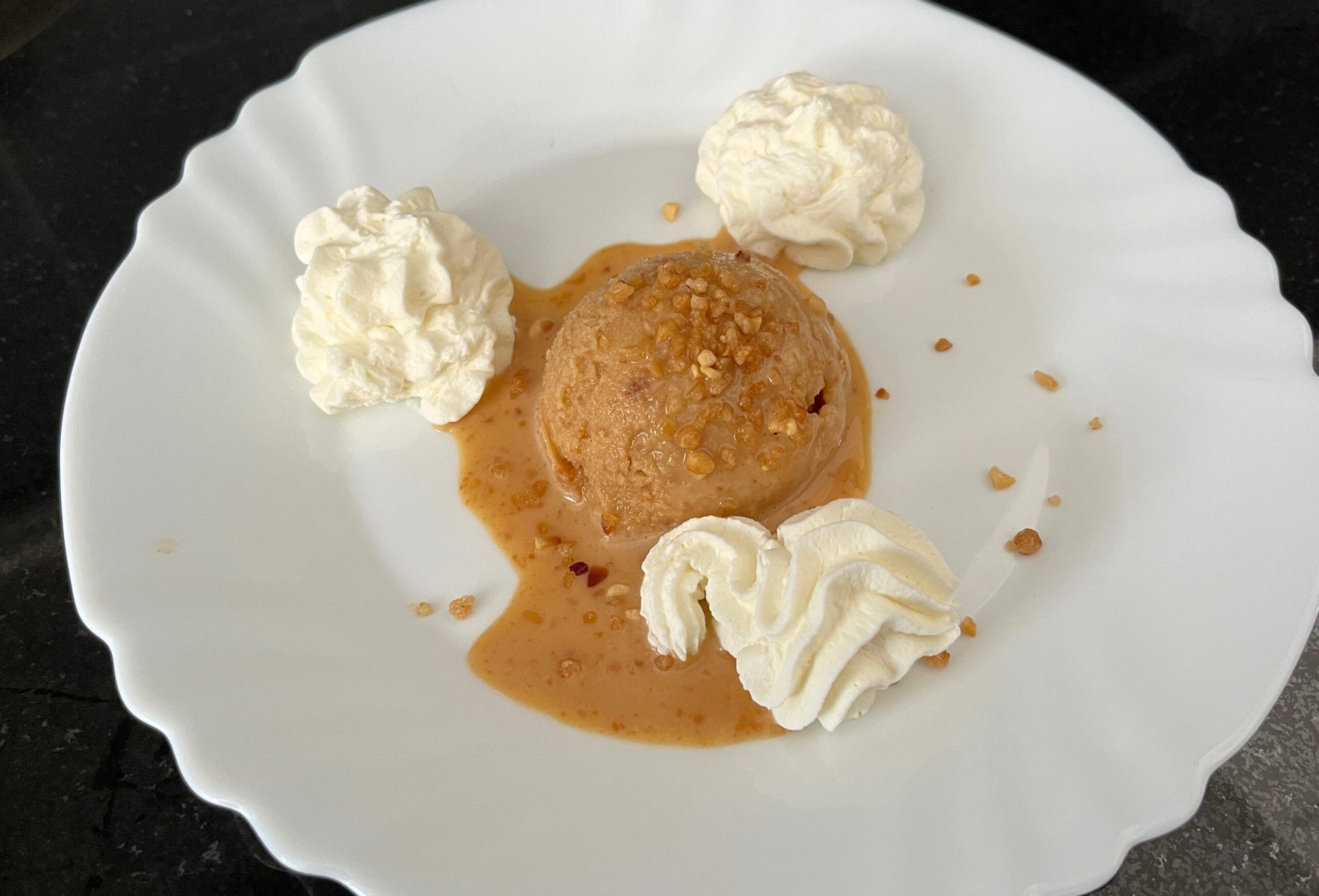 en un plato una bola de helado de turrón con nata montada y crocanti de almendra
