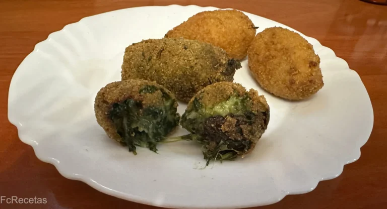 un plato blanco con croquetas de espinacas , una croqueta cortada por la mitad