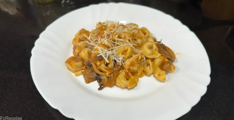 listo para servir un plato blanco con tortellini con salsa de tomate y champiñones, con queso parmesano rallado encima