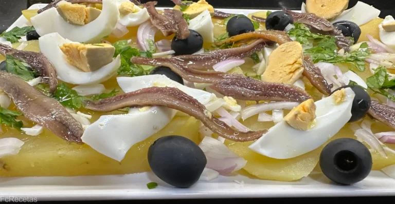 una ensalada de patatas y anchoas con huevo duro y olivas negras en una fuente blanca rectangular